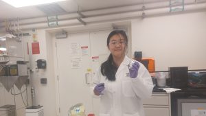 Caroline Song in a lab coat and gloves holding objects