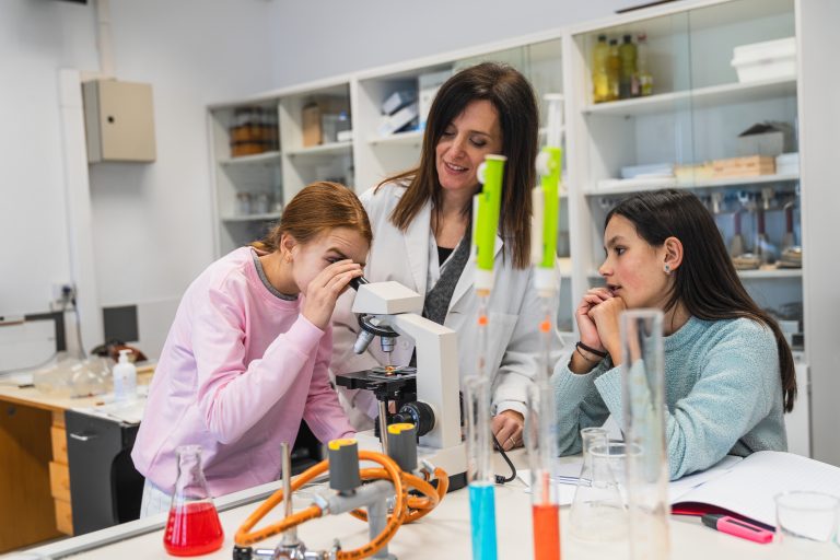 High,School,Students,Conducting,Scientific,Experiment,Using,Microscope,With,Teacher