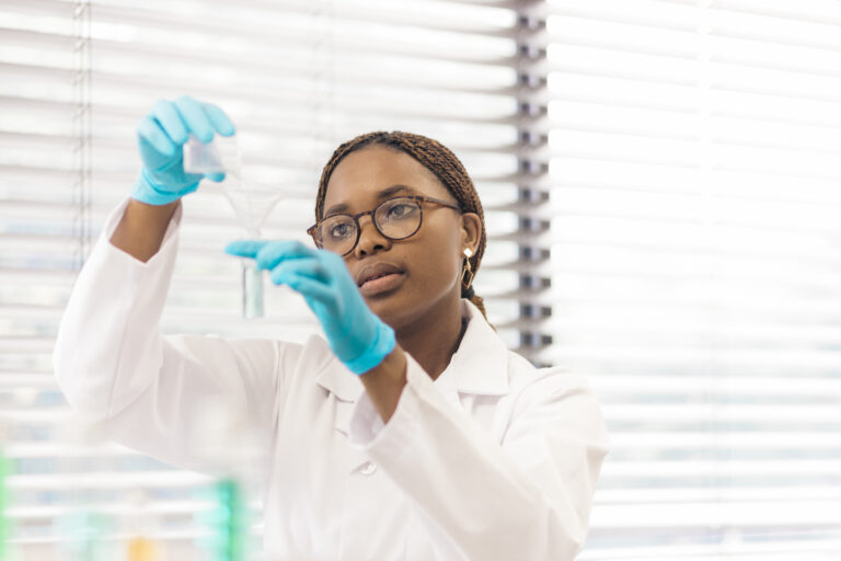 Young female scientist test tube and beaker making test in lab. Woman doctor doing research in clinical laboratory.